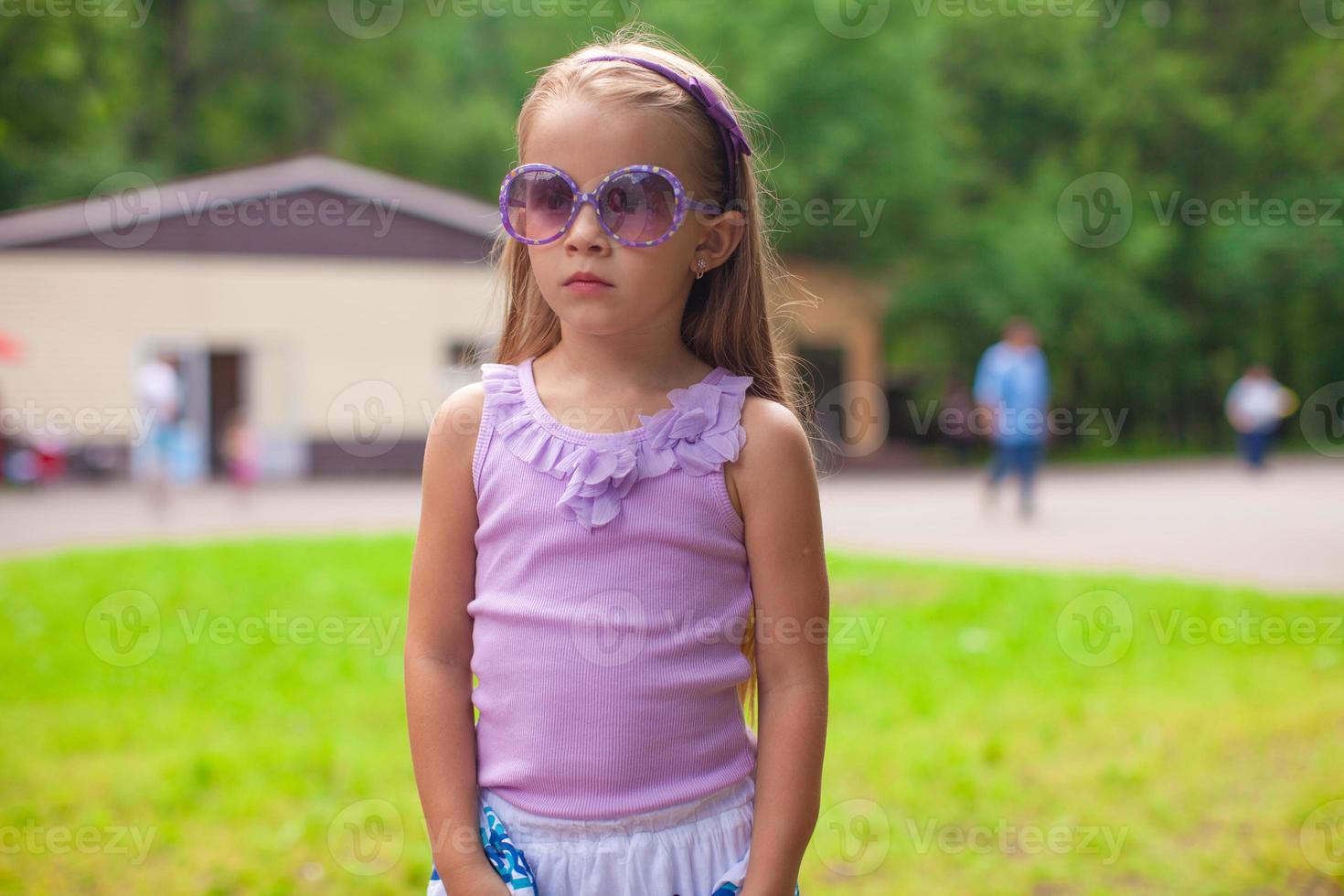 Wonderful little girl in sunglasses walking at summer park photo