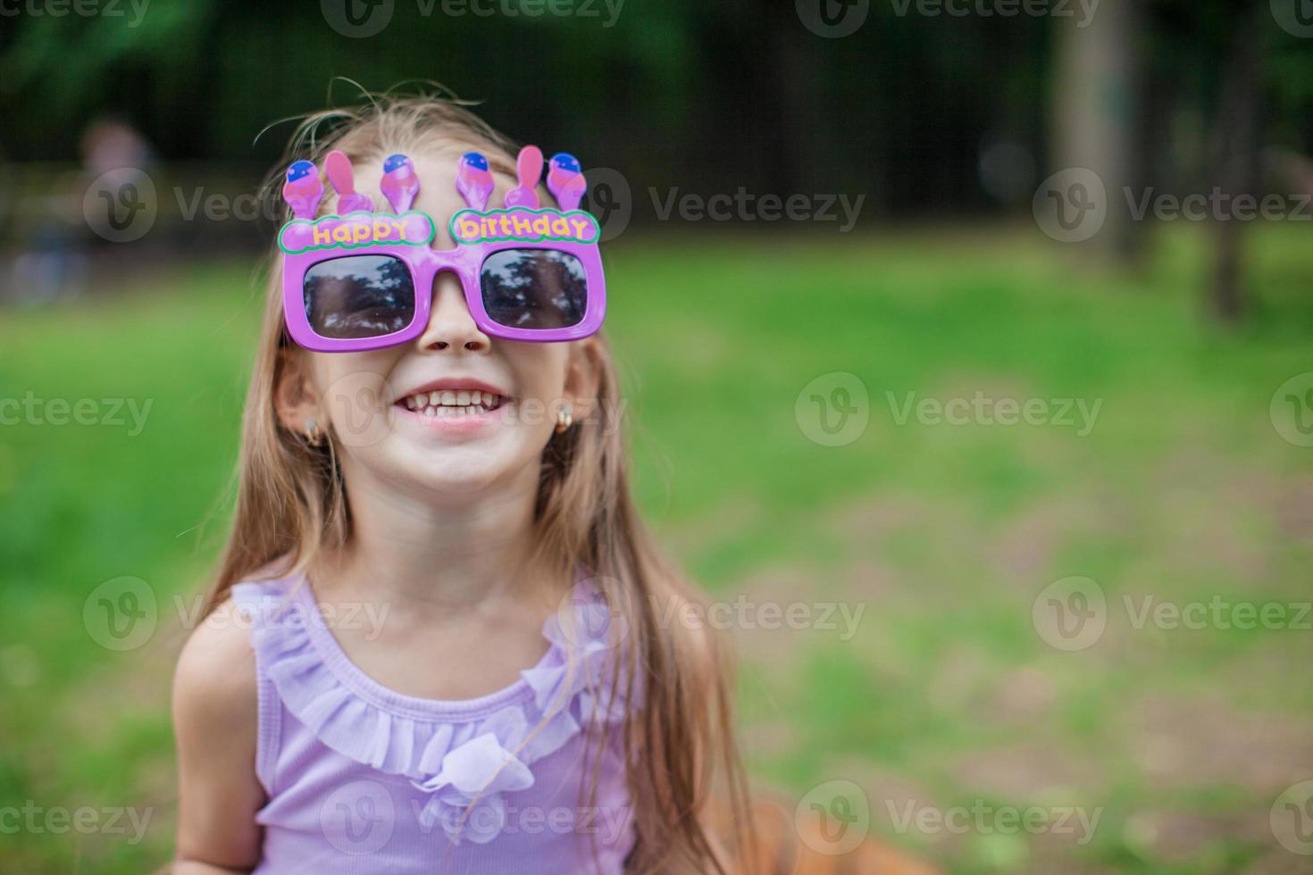 Adorable little girl in Happy Birthday glasses smiling outdoor photo