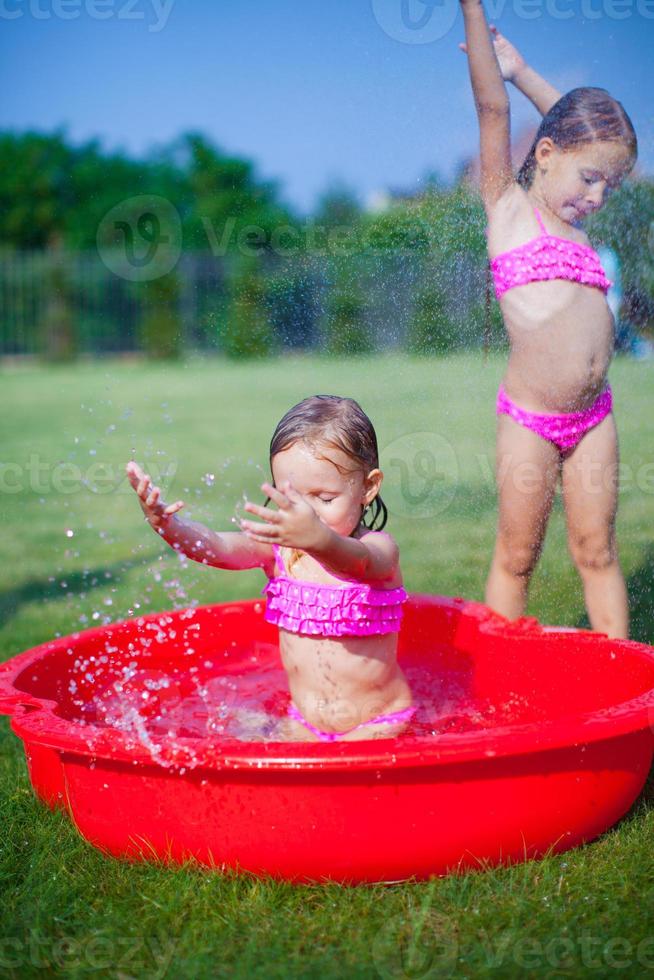 Two little sisters frolicing and splashing in their yard in small pool photo