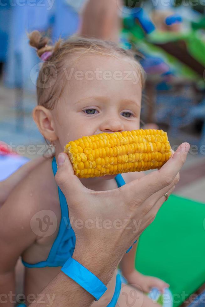 Young father feeds his little daughter corn near the swimming pool photo