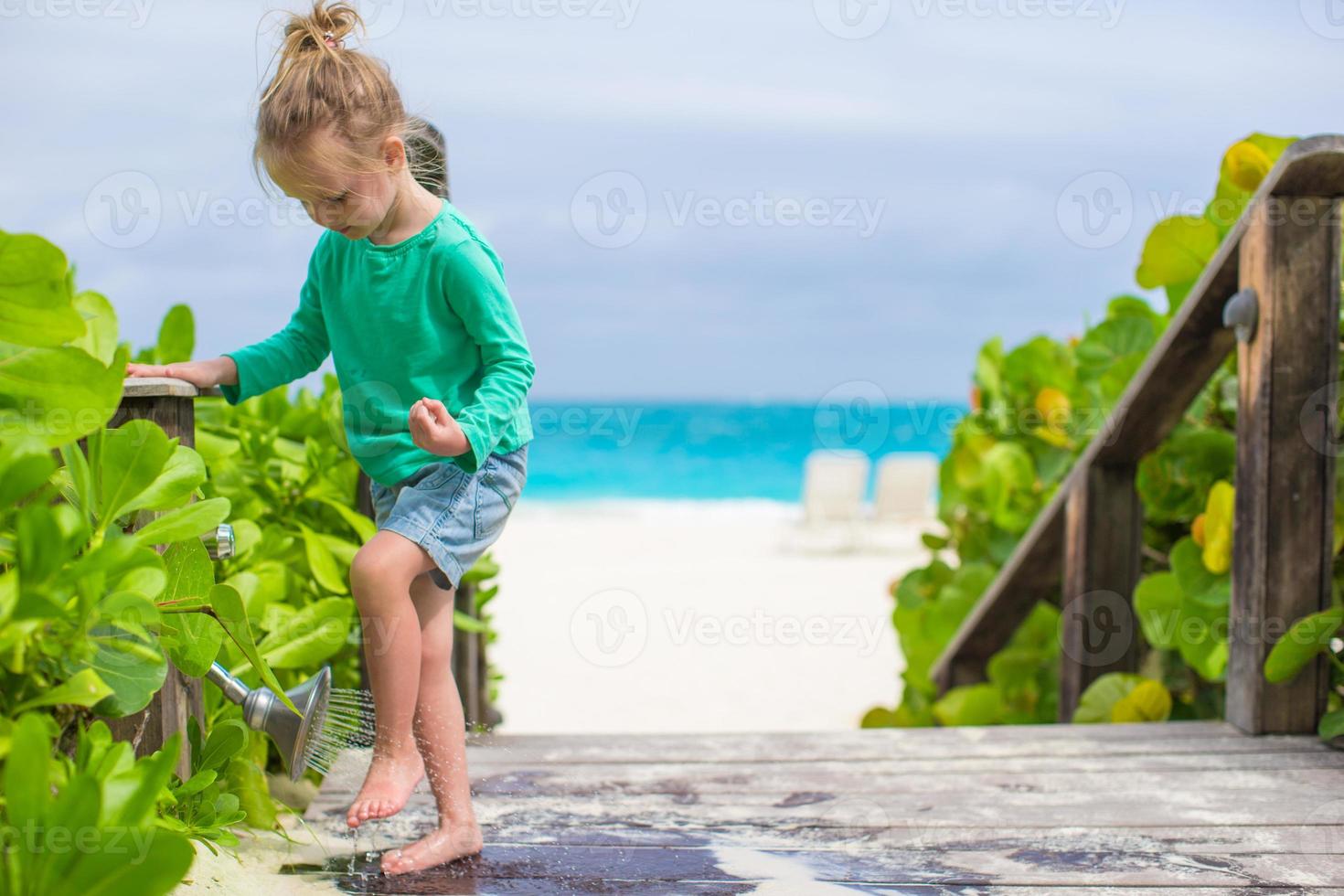 una niña linda lava la arena de sus pies en una playa tropical foto