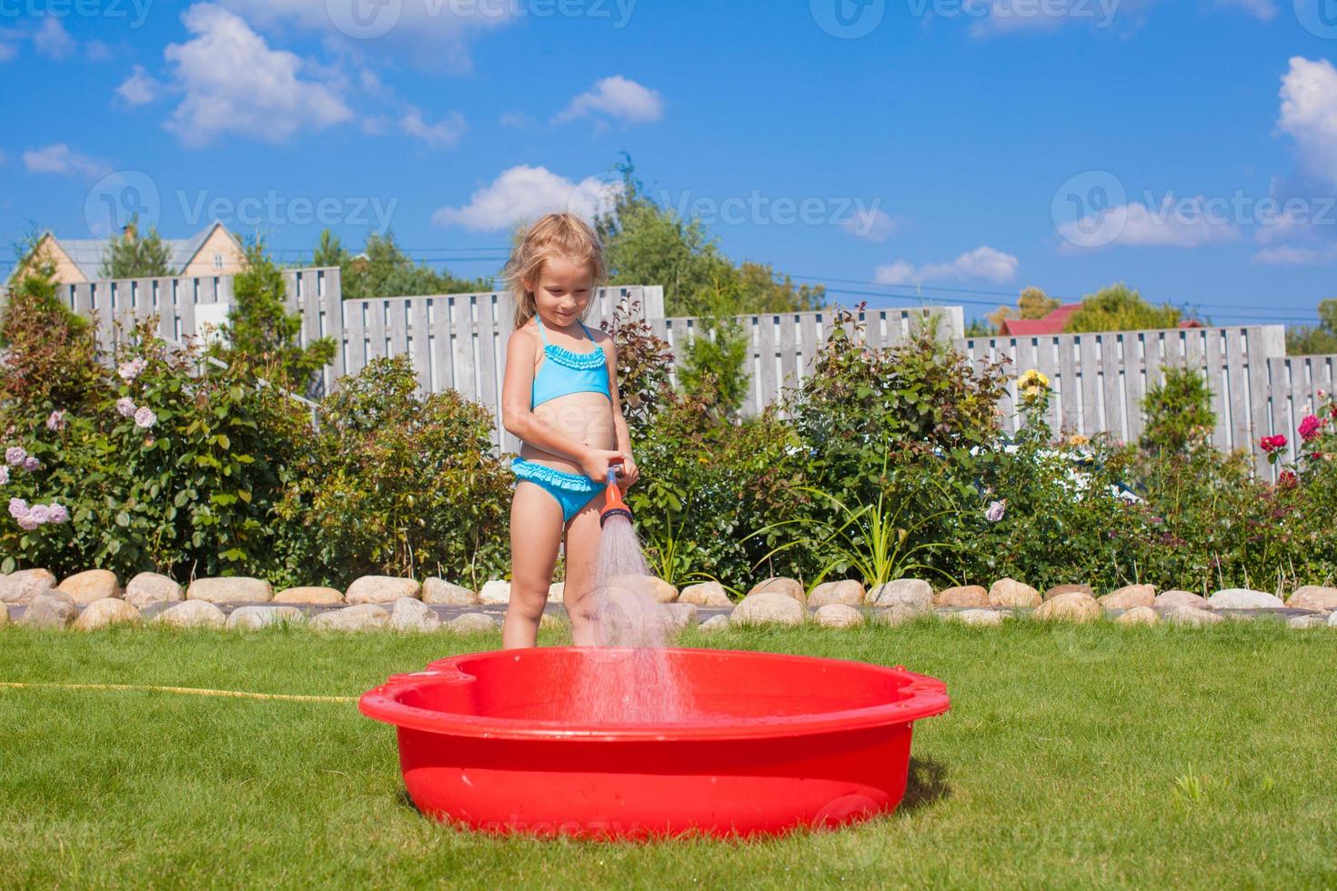 happy little girl pouring water from a hose and laughing photo