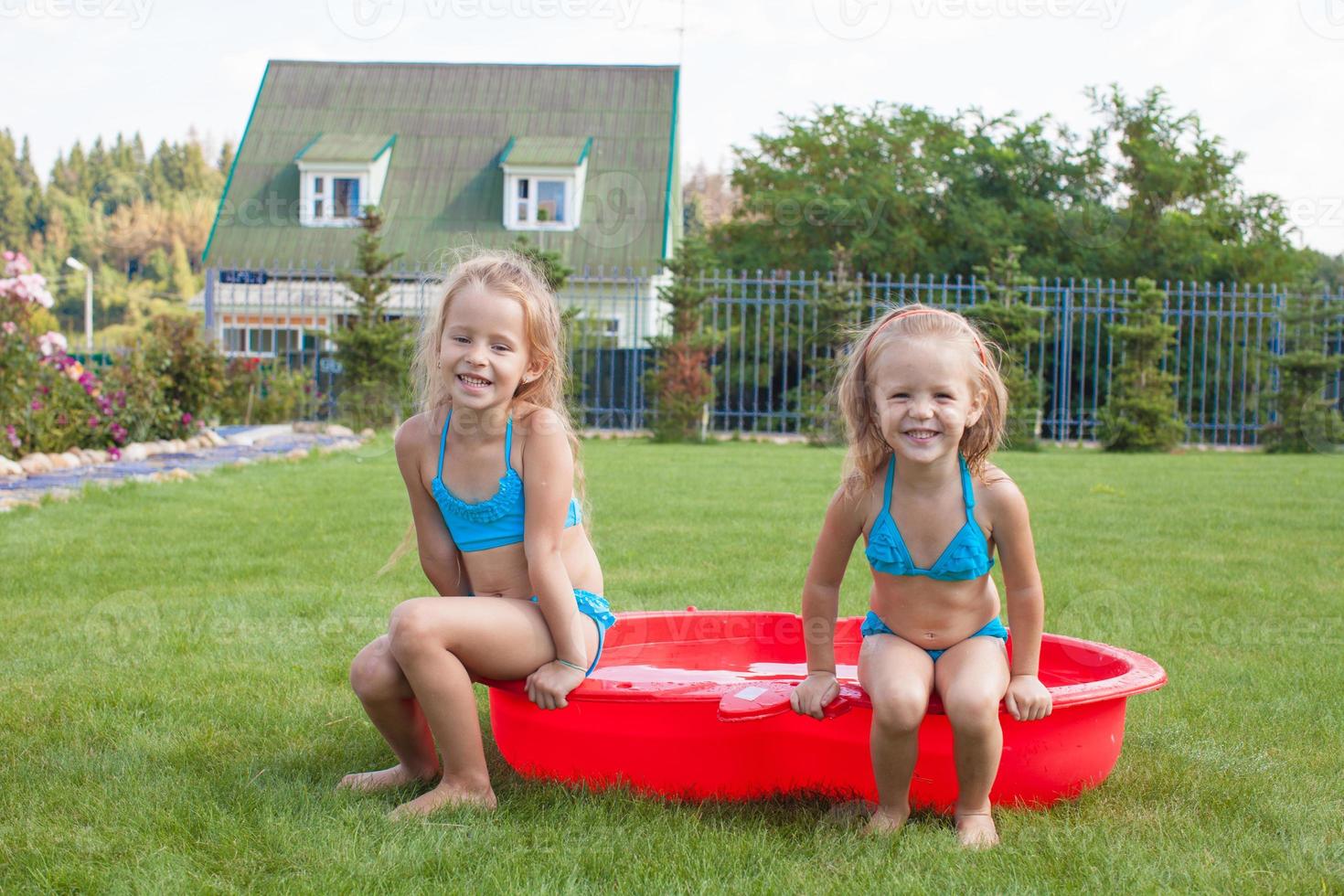 Two little sisters sitting in their yard in small pool photo