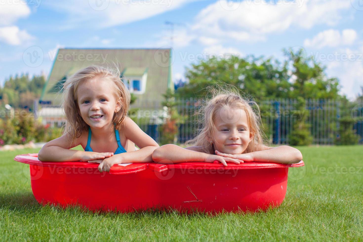Two little sisters frolicing and splashing in their yard in small pool photo