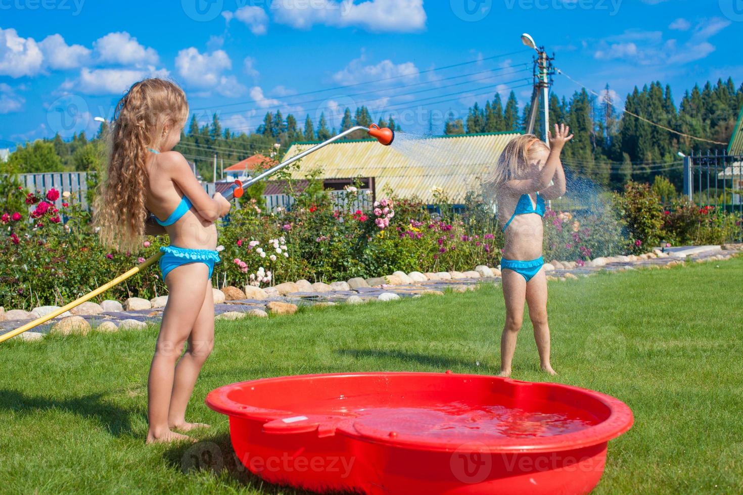 Two little sisters frolicing, splashing and having fun in their yard photo