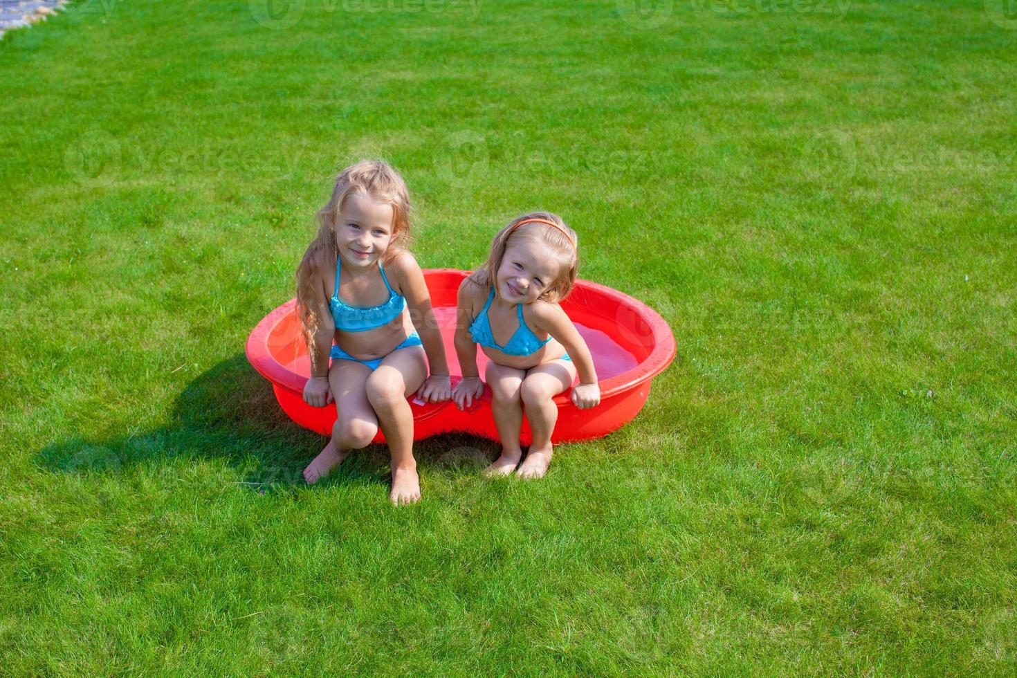 Two little sisters frolicing and splashing in their yard in small pool photo