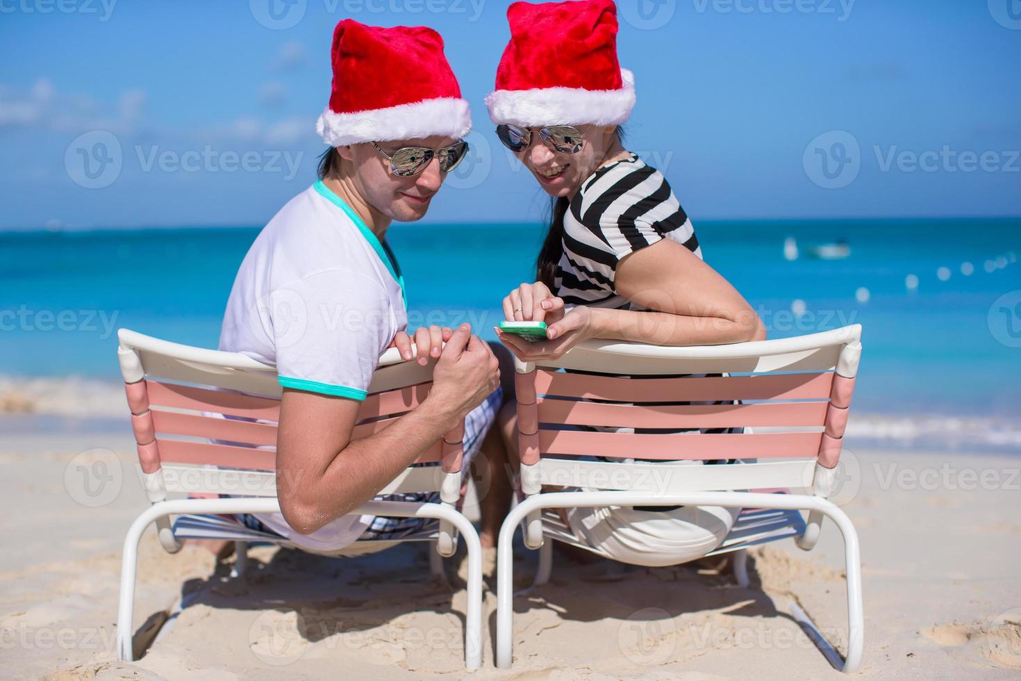 Family of two in Santa hats sitting on beach chair photo