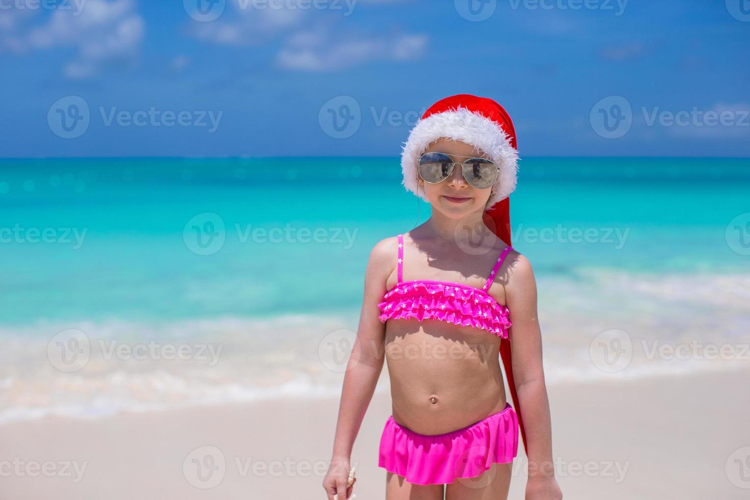 Little cute girl in red Santa hat on tropical beach photo