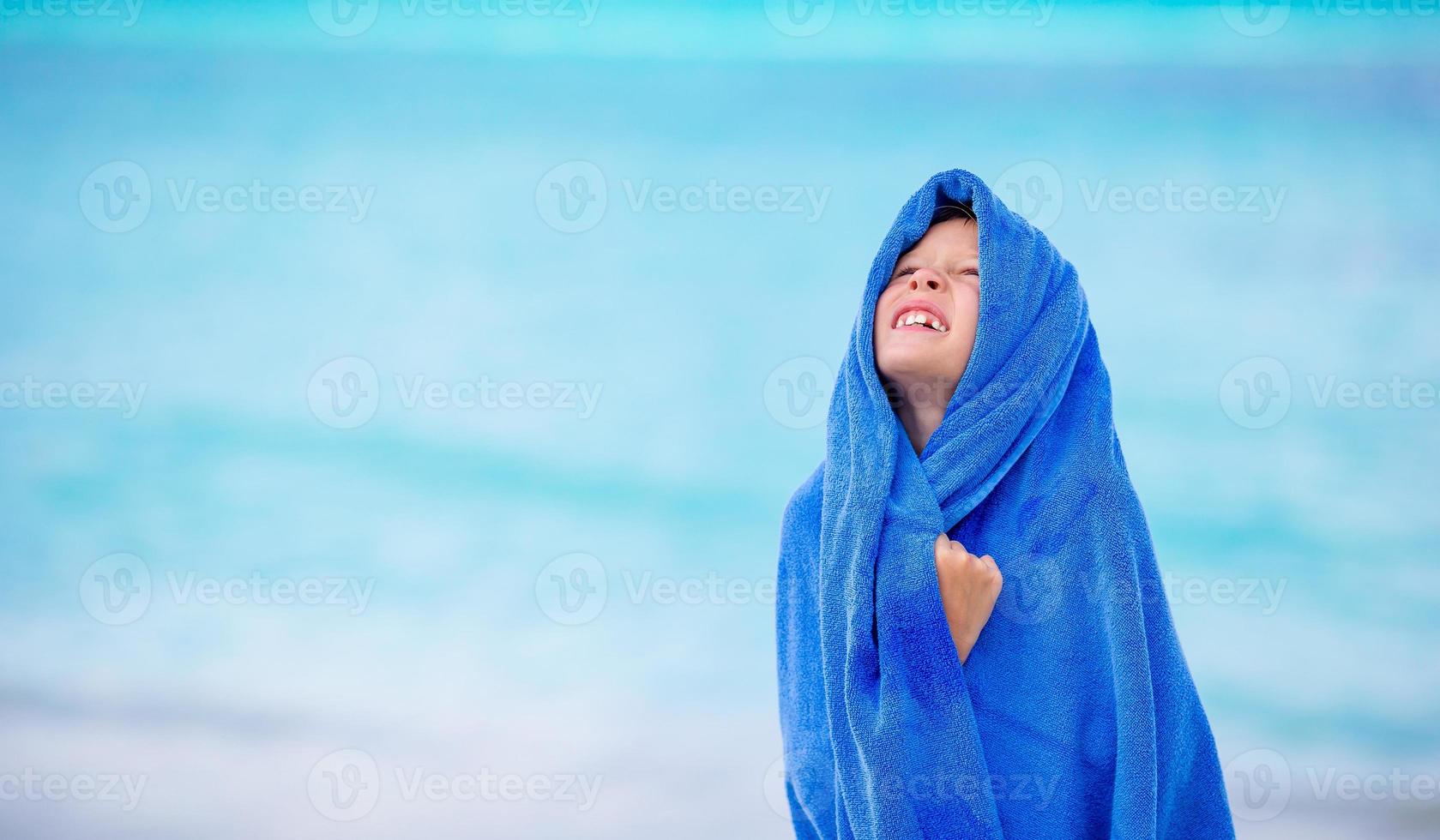 Adorable little girl wrapped in towel at tropical beach after swimming in the sea photo