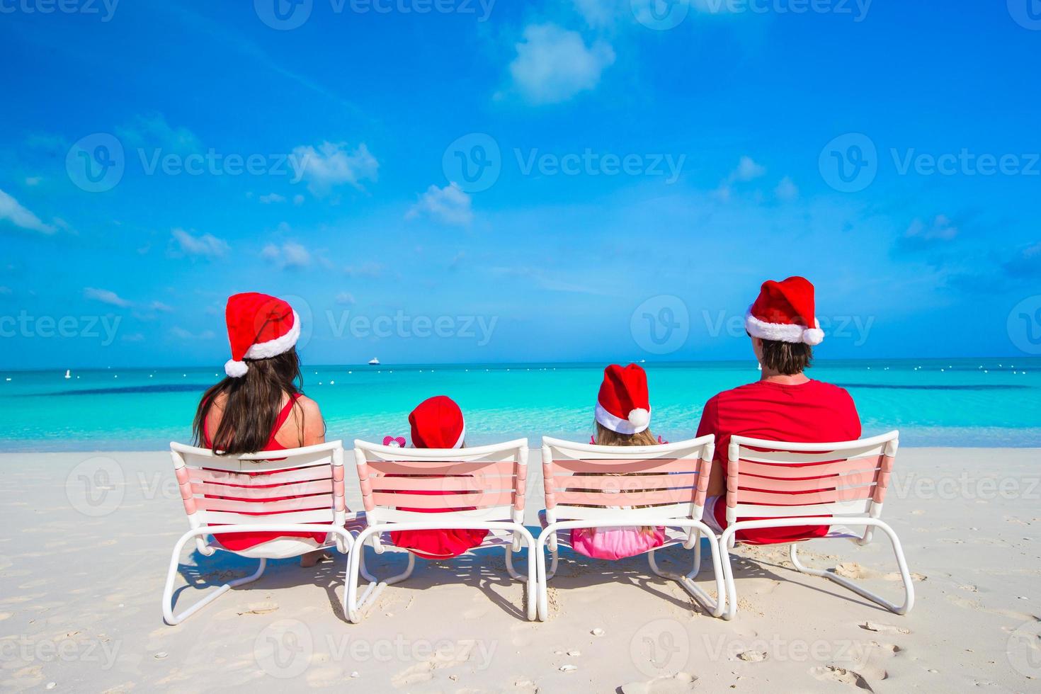 Happy family of four on beach in red Santa hats photo