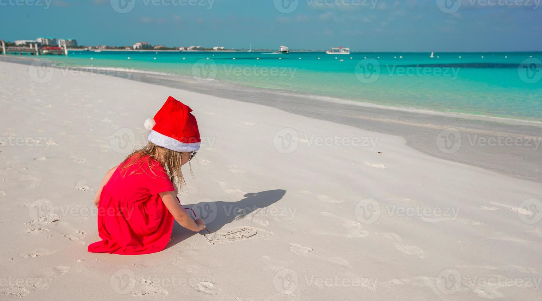 Little cute girl in red Santa hat playing on the beach photo