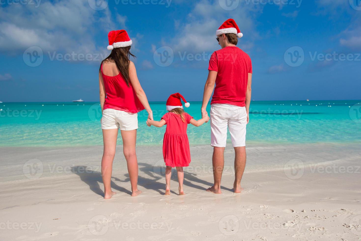 familia feliz con sombreros de santa divirtiéndose en la playa blanca foto