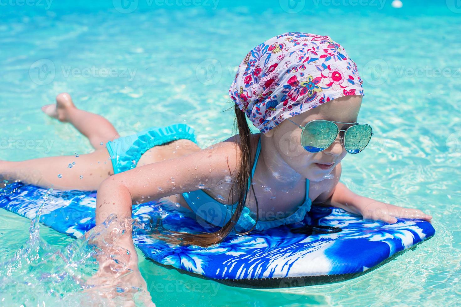 Little adorable girl on a surfboard in the turquoise sea photo