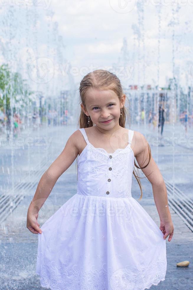 Little cute girl have fun in open street fountain at hot summer day photo
