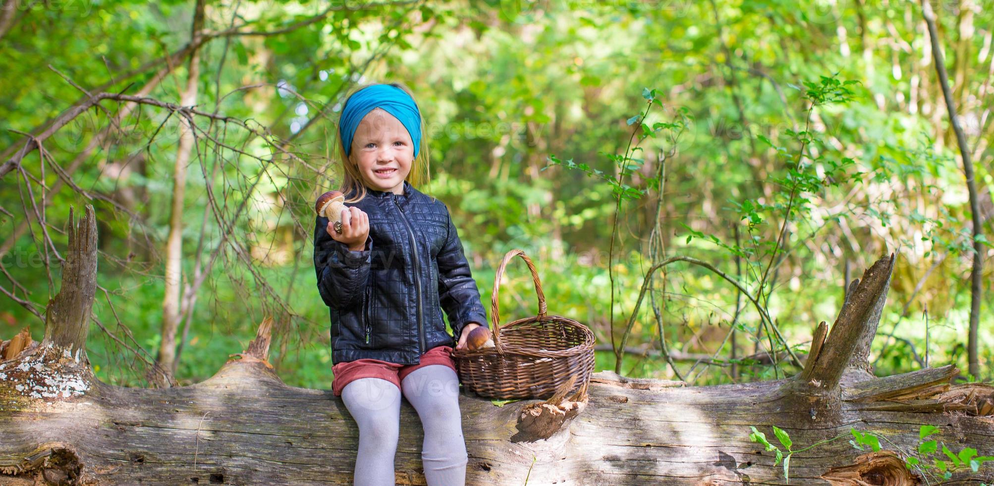 Little adorable girl gathering mushrooms in an autumn forest photo