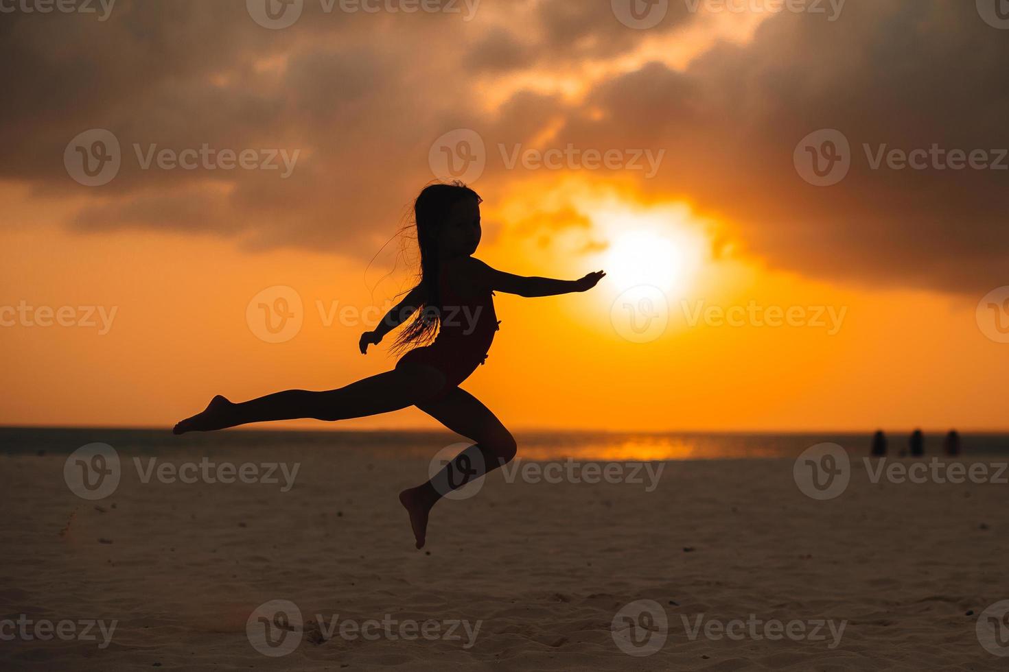 Adorable happy little girl on white beach at sunset. photo