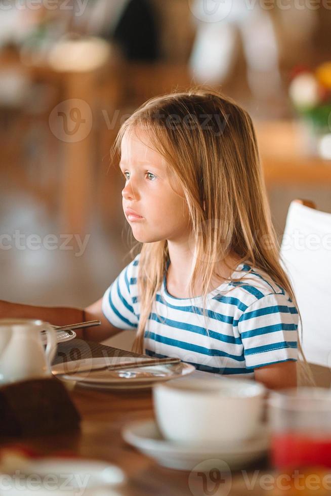 Adorable little girl having breakfast at outdoor cafe photo