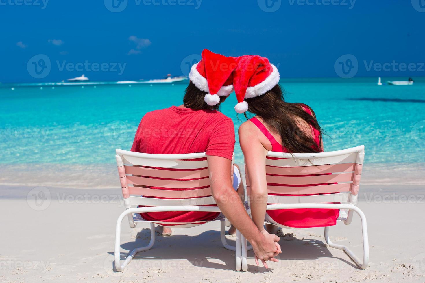 feliz pareja romántica con sombreros rojos de santa en la playa tropical foto