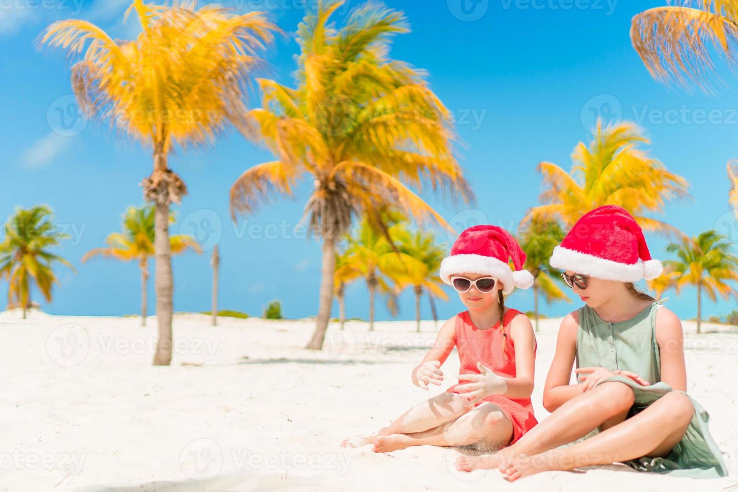 Little adorable girls in Santa hats during beach vacation have fun together photo