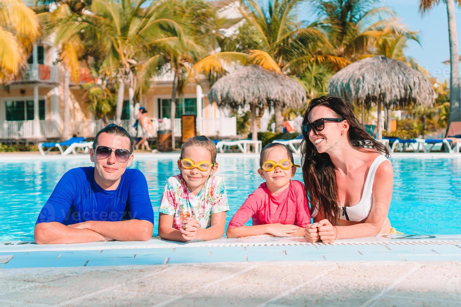 Happy family of four in outdoors swimming pool photo