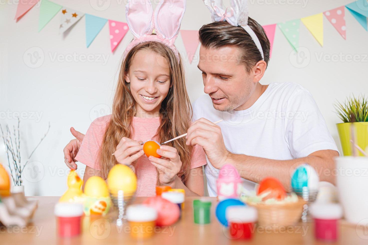 Father and his little daughter painting eggs. Happy family preparing for Easter. photo