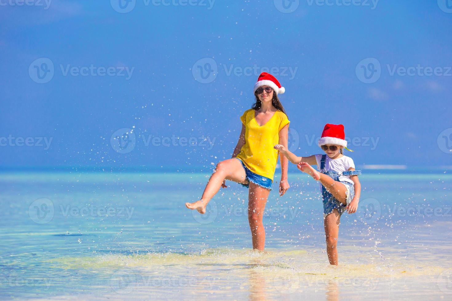 niña y madre joven con sombrero de santa durante las vacaciones en la playa foto