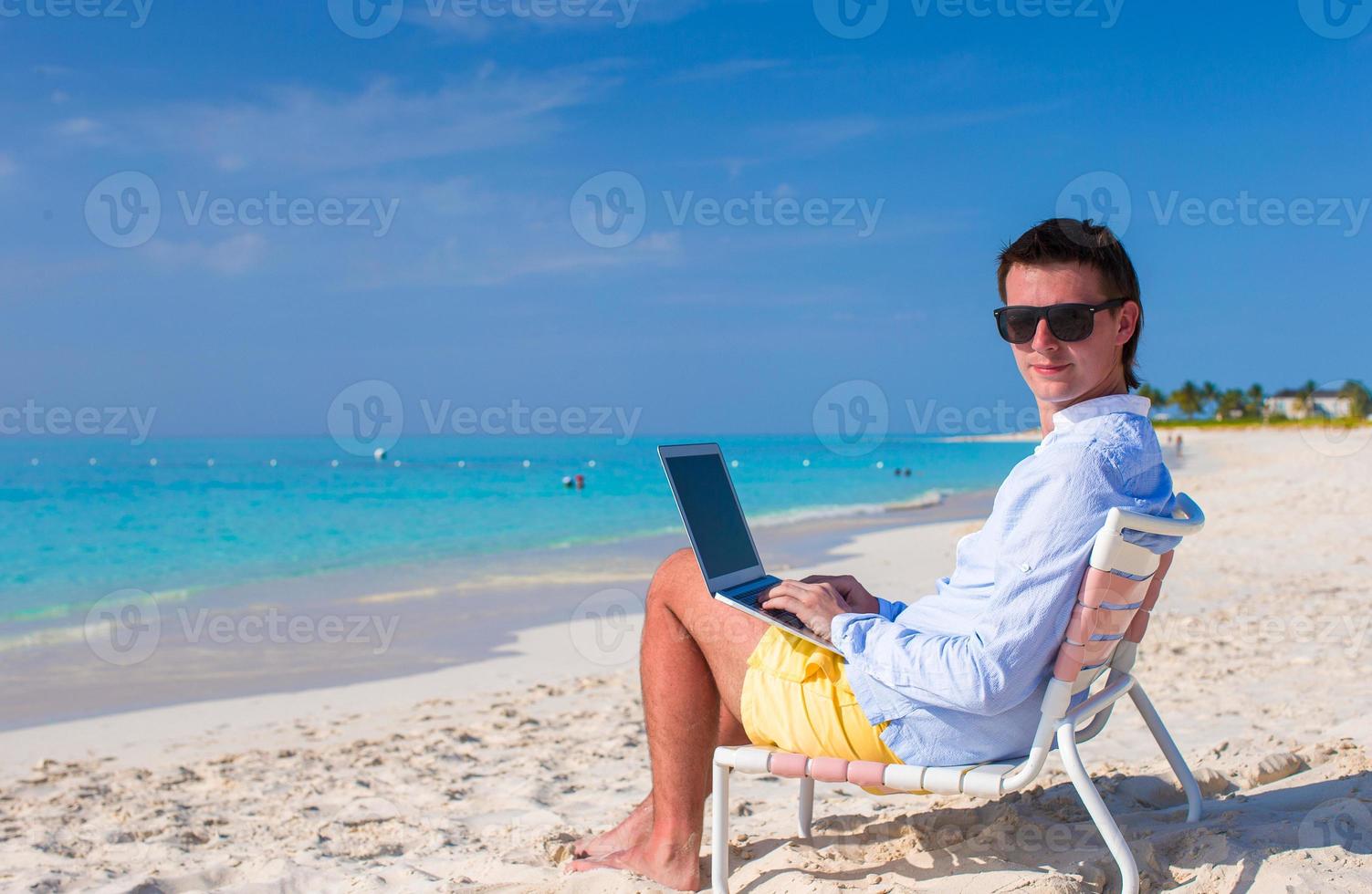 Young man with laptop and cell phone on tropical beach photo