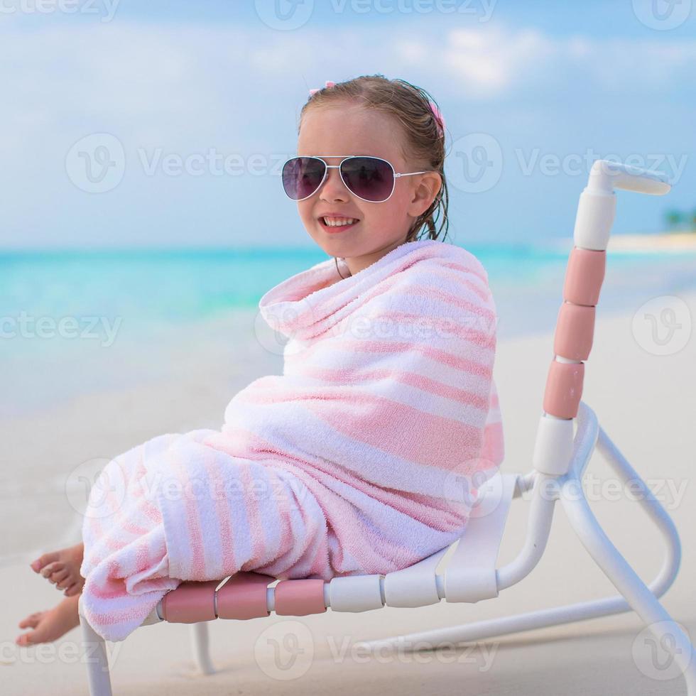 Adorable little girl in sunglasses covered with towel at tropical beach photo