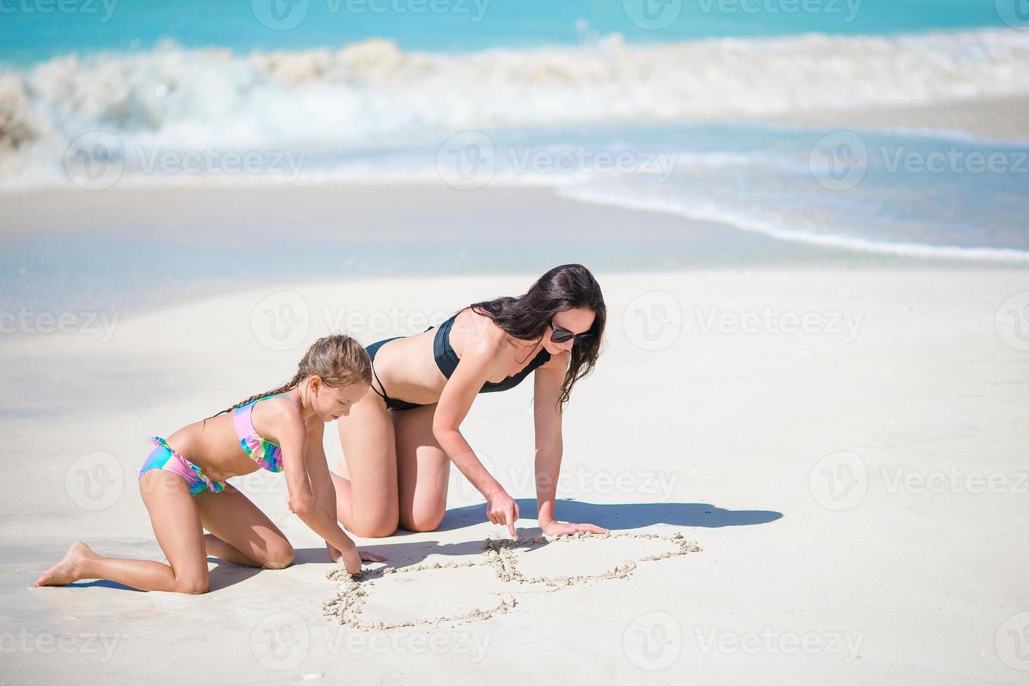 Mother and little kid drawing on sandy beach photo