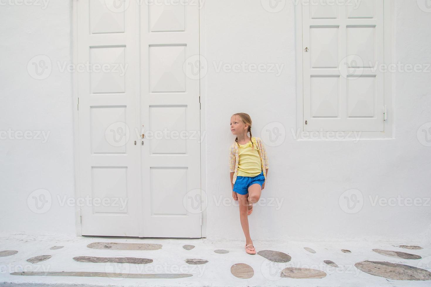 retrato de niña al aire libre en el antiguo pueblo griego. niño en la calle del pueblo griego con paredes blancas y puertas coloridas foto