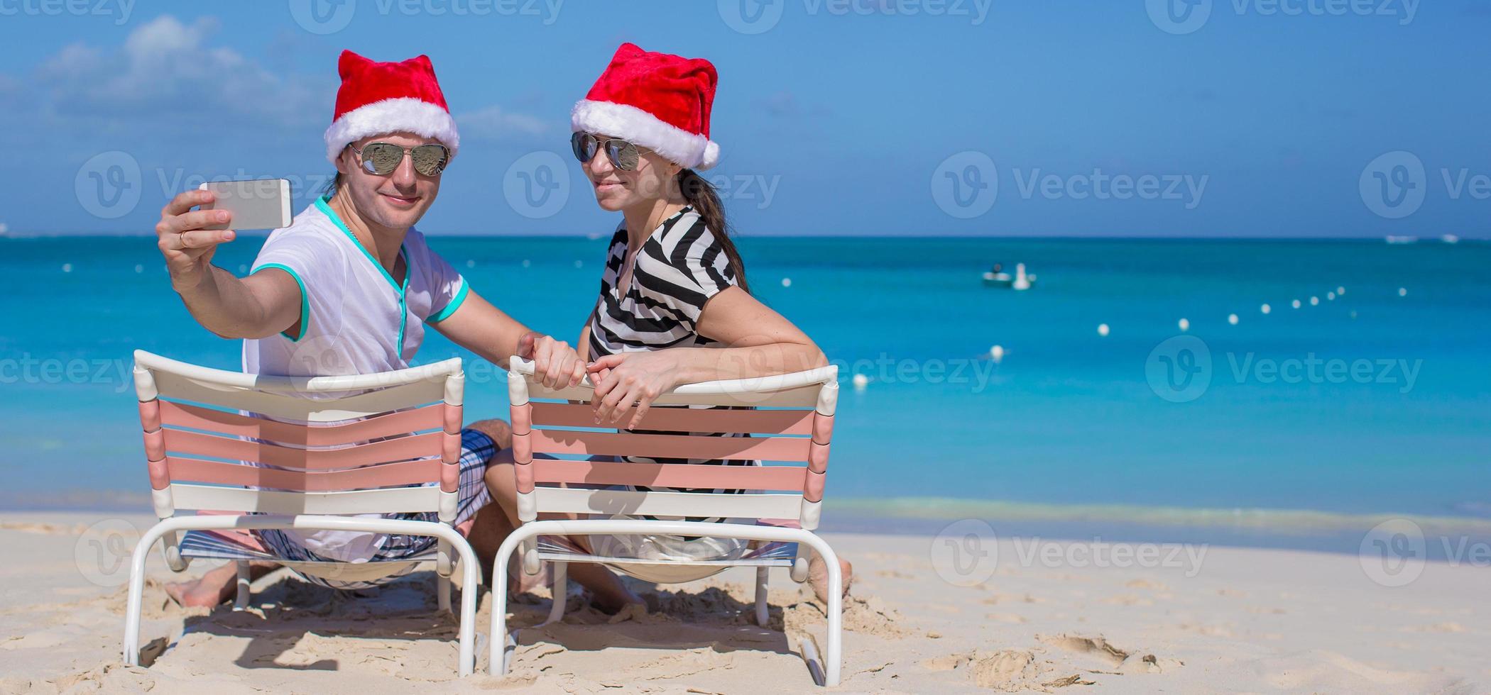 joven pareja feliz con sombreros rojos de santa tomando una foto en el teléfono celular