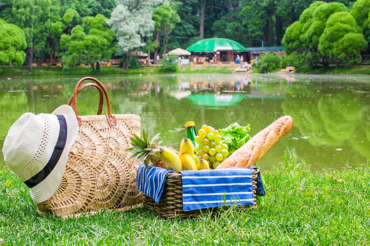 Picnic basket with fruits, bread and hat on straw bag photo