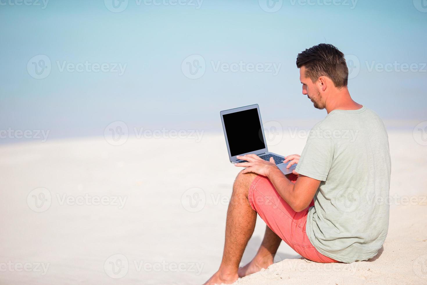 Young man with tablet computer during tropical beach vacation photo