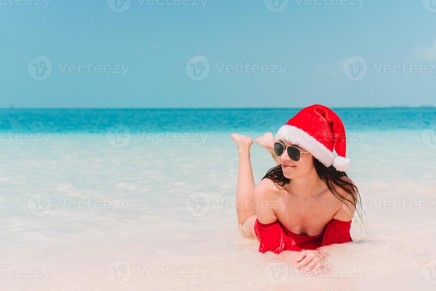 Young woman in Santa Hat walking spread her hands on white sandy beach photo
