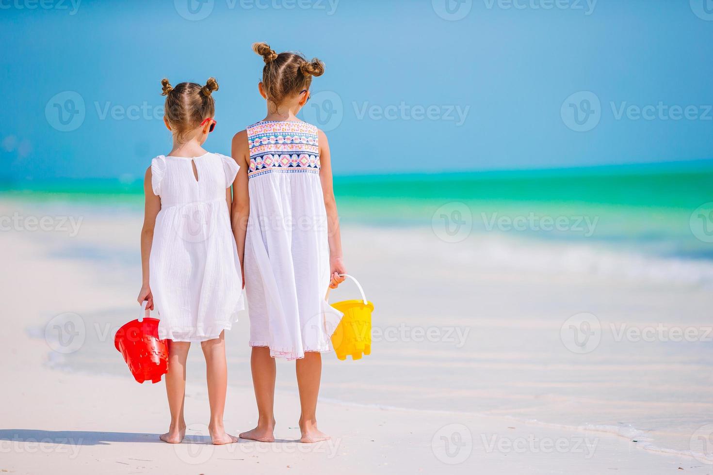 Little happy funny girls have a lot of fun at tropical beach playing together. Sunny day with rain in the sea photo