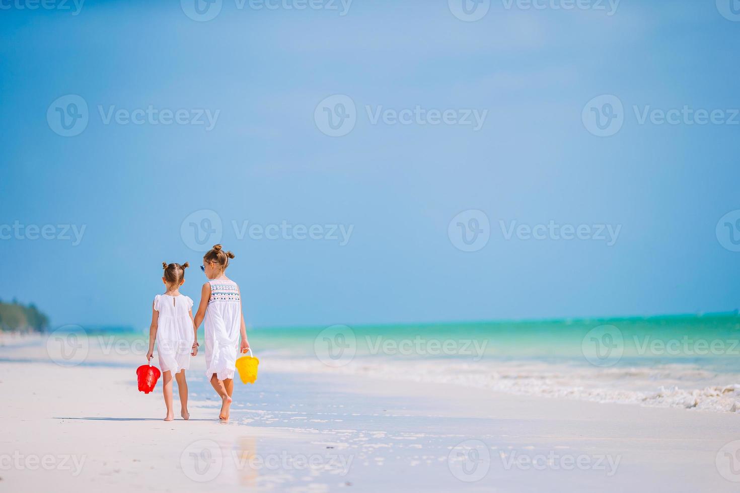 Little happy funny girls have a lot of fun at tropical beach playing together. Sunny day with rain in the sea photo