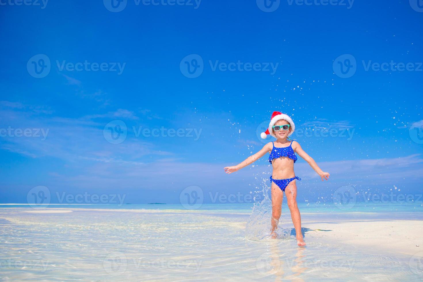 Little happy girl in Santa hat during beach vacation on Maldives photo