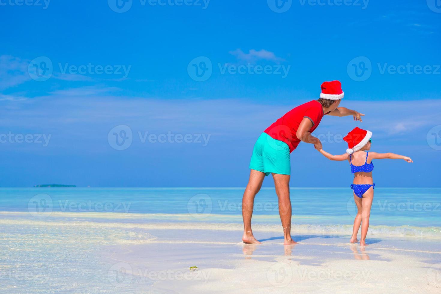 niña y padre feliz en sombrero de santa durante las vacaciones de navidad en la playa foto
