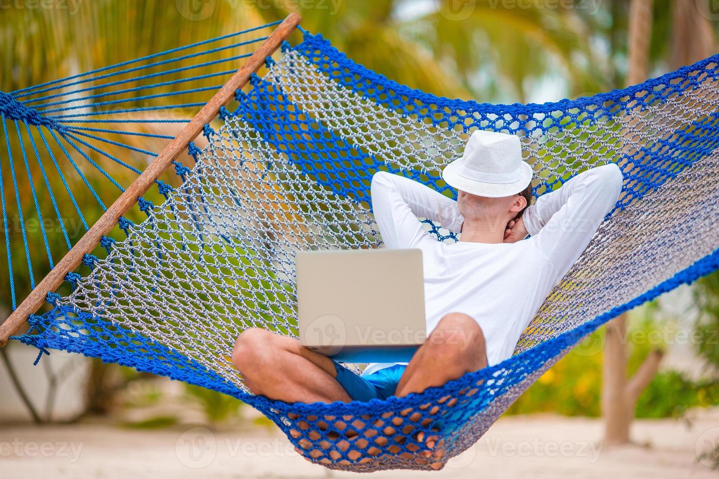 Young man with laptop at hammock on tropical vacation photo