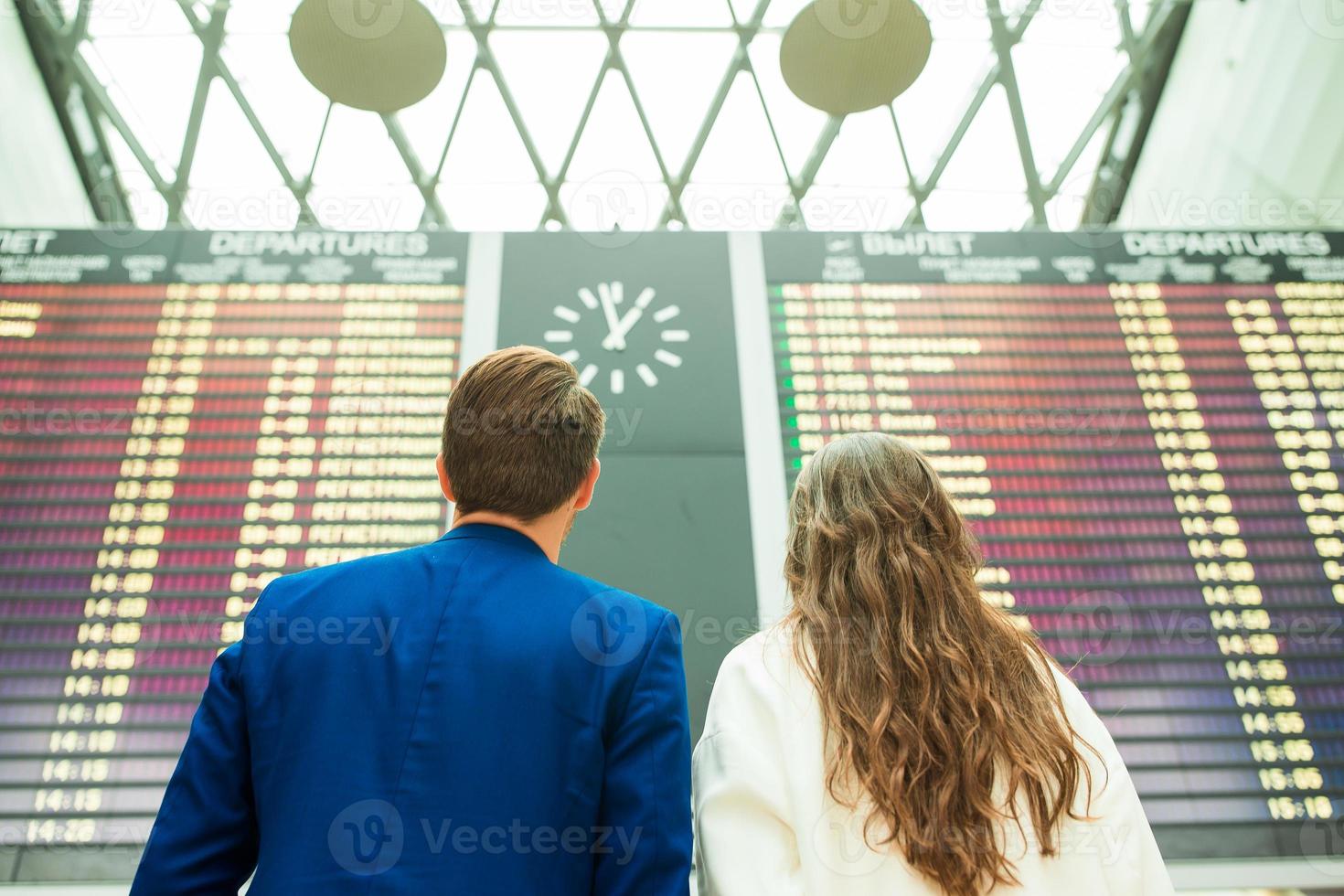 joven y mujer en el aeropuerto internacional mirando el tablero de información de vuelo foto