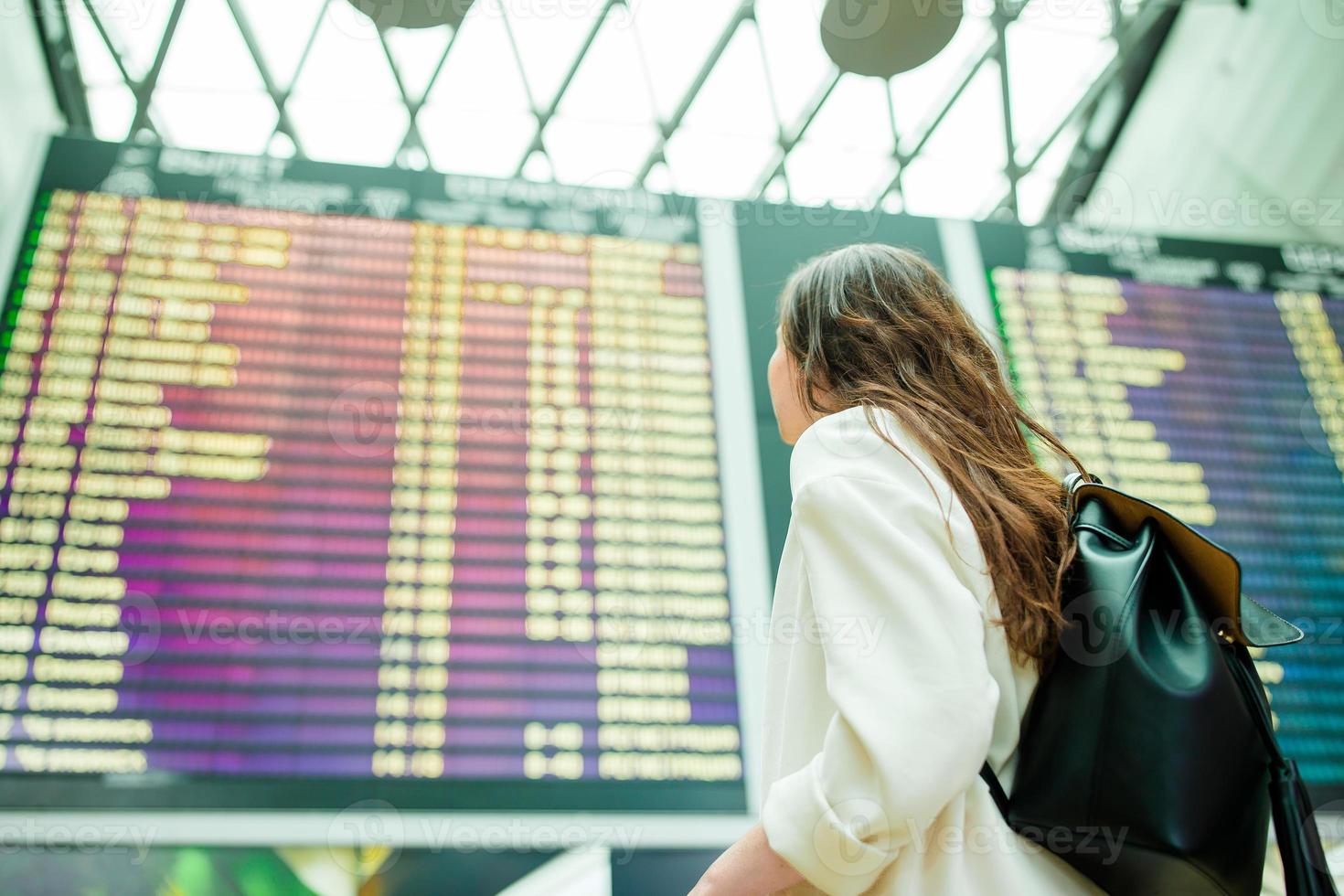 vista trasera de una mujer en el aeropuerto internacional mirando el tablero de información de vuelo comprobando el vuelo foto