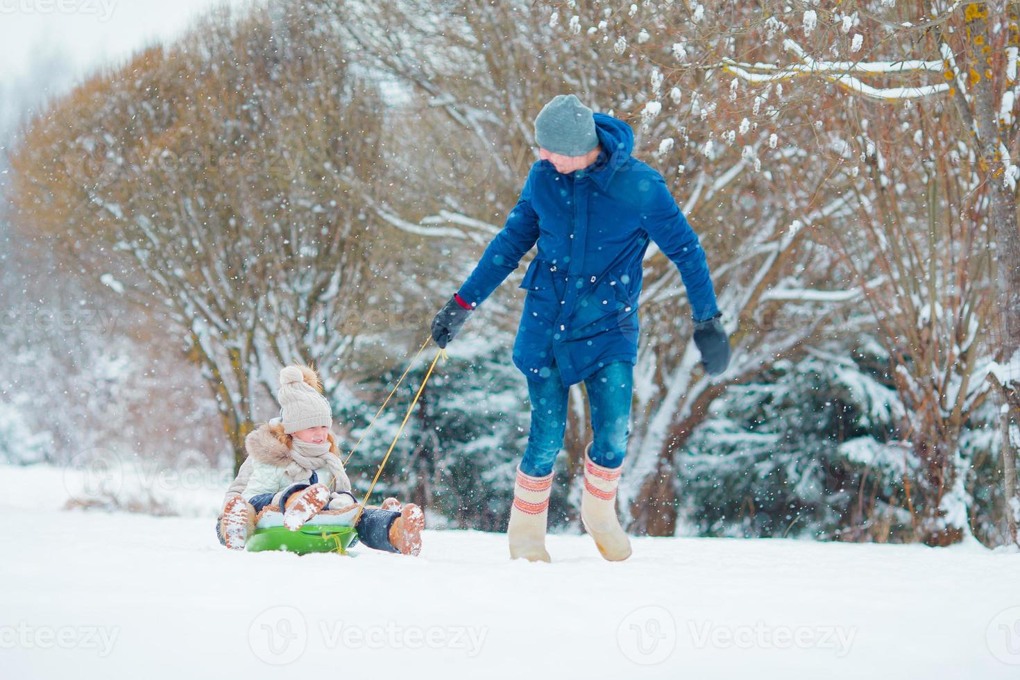 Little girls enjoying sledding in winter day. Father sledding his little adorable daughters. Family vacation on Christmas eve outdoors photo