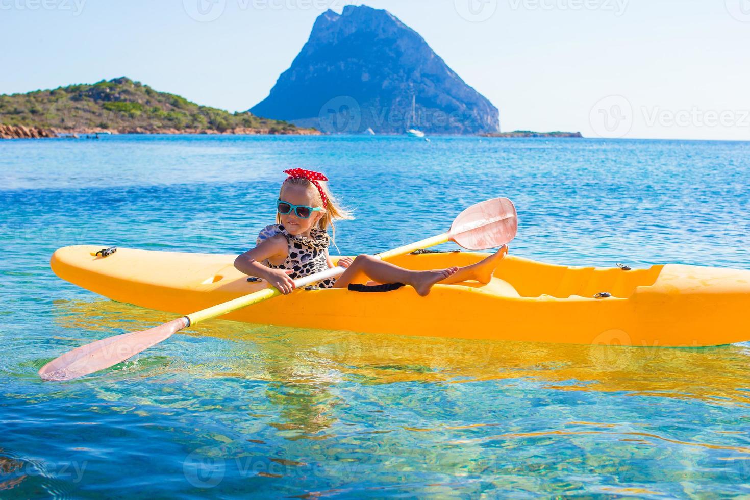 una niña linda disfruta nadando en un kayak amarillo en aguas turquesas claras foto