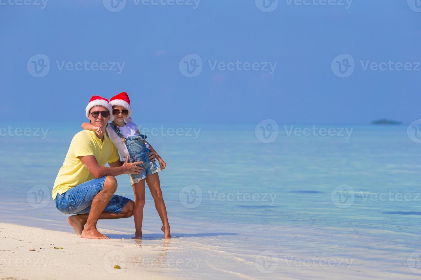 niña y padre feliz en sombrero de santa durante las vacaciones de navidad en la playa foto