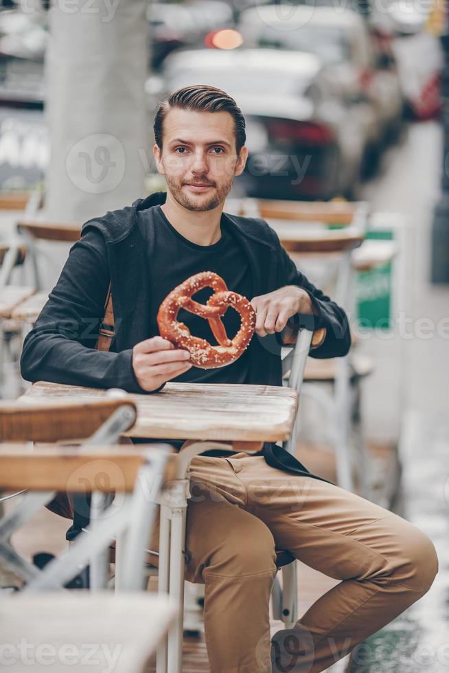 Beautiful young man holding pretzel and relaxing in park photo