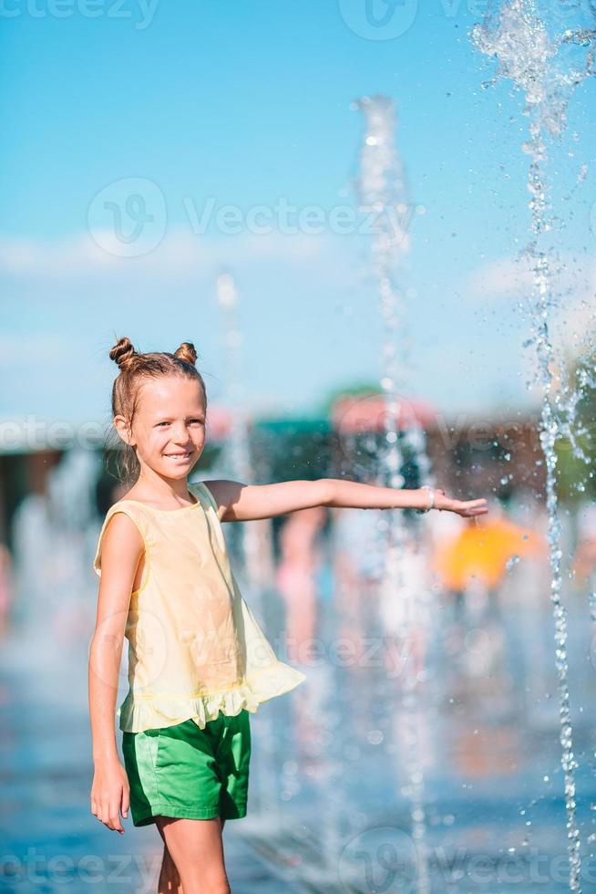 Little adorable girl have fun in street fountain at hot sunny day photo
