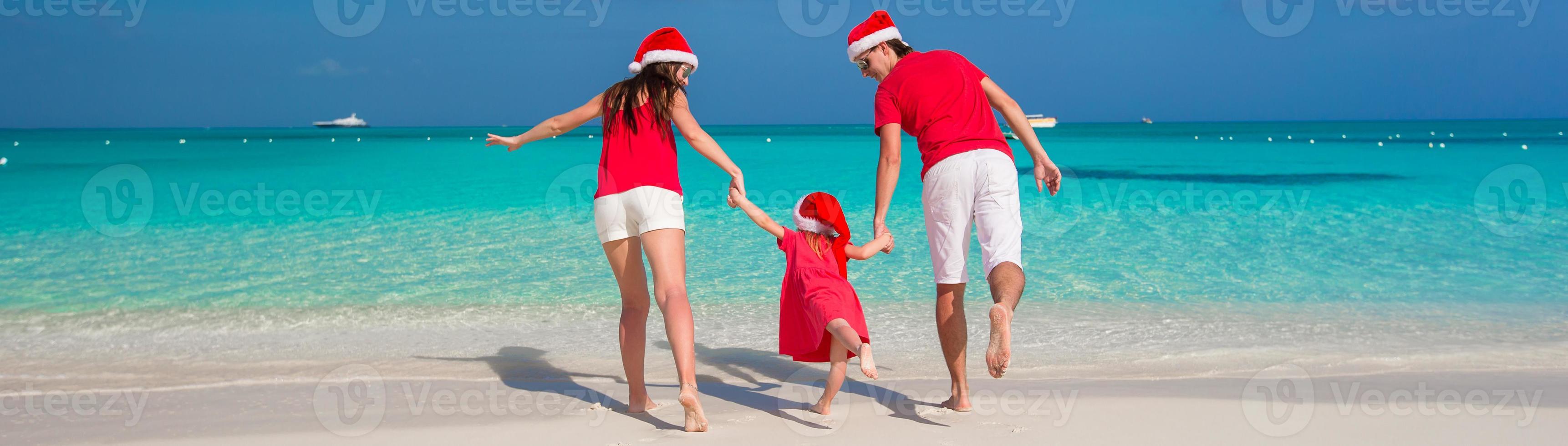 Happy family in Christmas Hats having fun on white beach photo