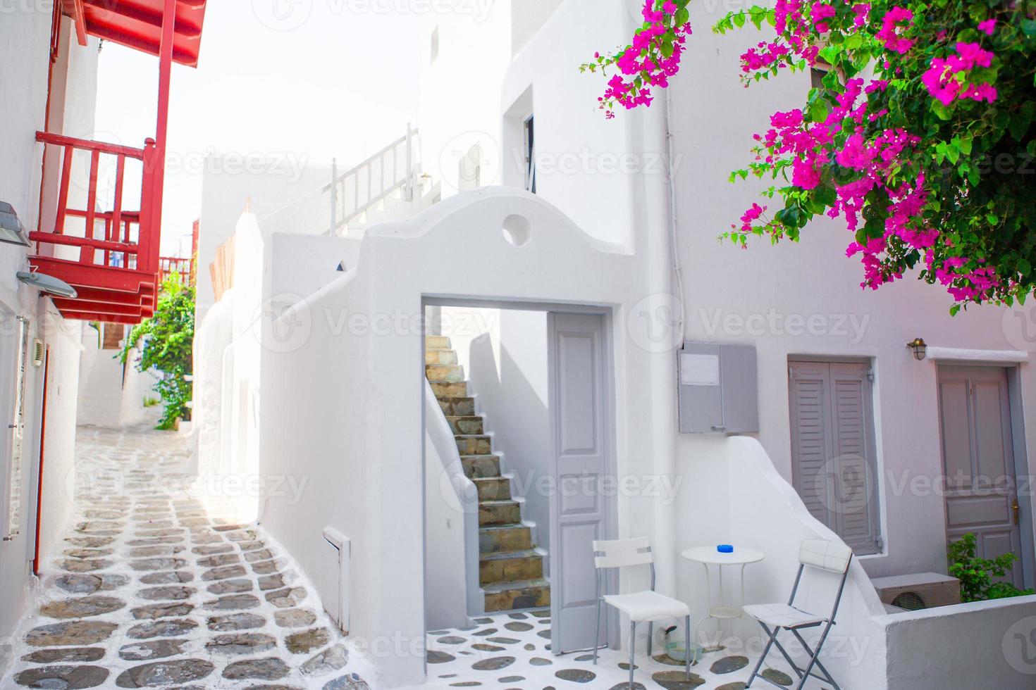 The narrow streets with blue balconies, stairs, white houses and flowers in beautiful village in Greece. Beautiful architecture building exterior with cycladic style in Mykonos photo