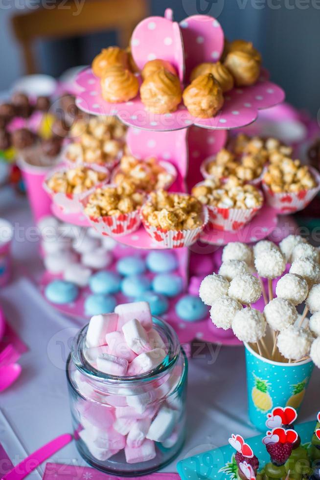 malvaviscos, merengues de colores dulces, palomitas de maíz, pasteles de crema pastelera y pasteles blancos en la mesa foto