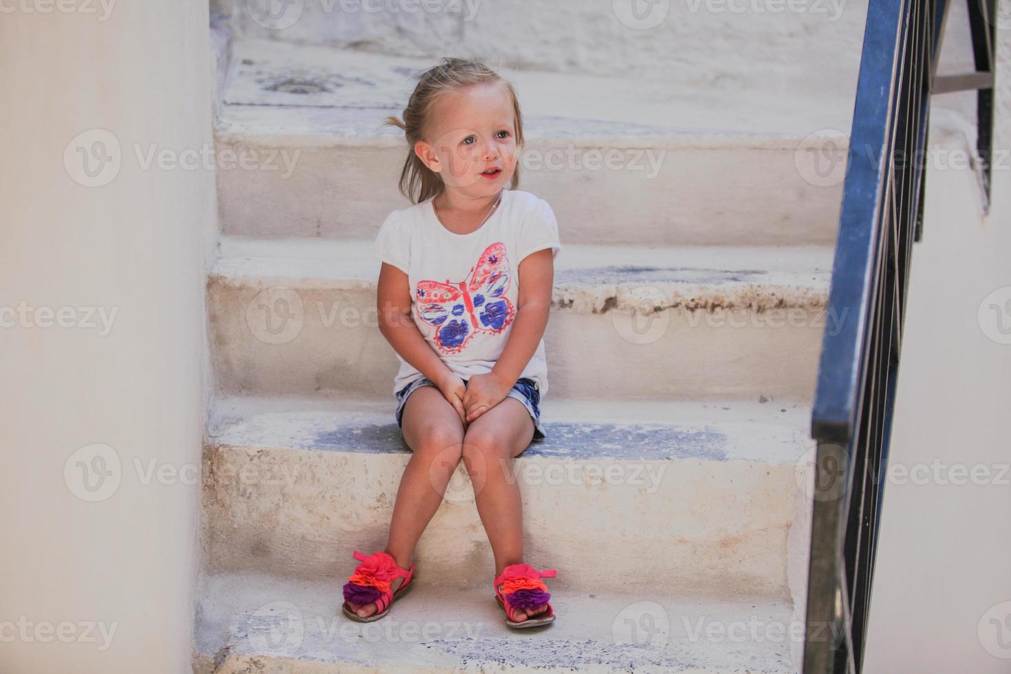 linda niña sentada en los escalones de la casa antigua en el pueblo de emporio, santorini, grecia foto